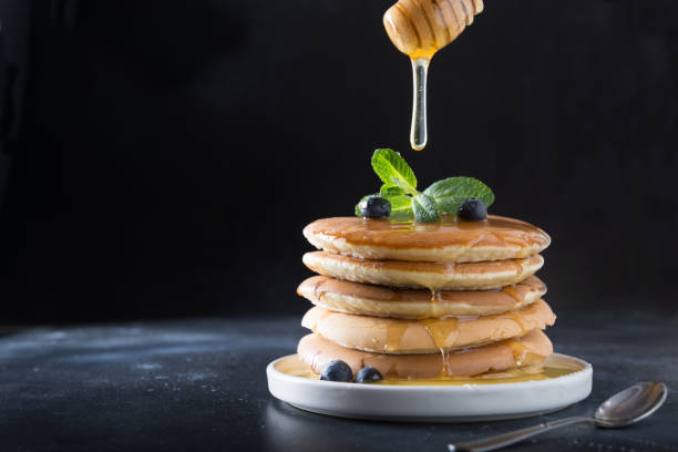 istock Stack of pancakes with pouring honey, fresh blueberry and mint on black. 1141292085