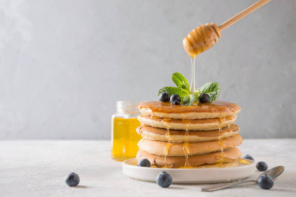 istock Stack of pancakes with pouring honey, fresh blueberry and mint on light background. 1141292088