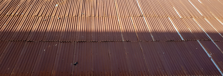 Old brown roof top, made of corrugated metal sheets, covered halfway by sunlight.