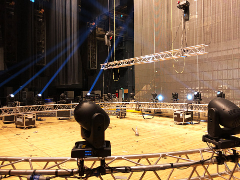 Installation of professional sound, light, video and stage equipment for a concert. Stage lighting equipment is clamped on a truss for lifting on led screen background.