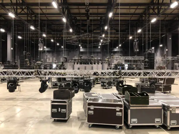 Photo of Installation of professional sound, light, video and stage equipment for a concert. Stage lighting equipment is clamped on a truss for lifting. Flight cases with cables.