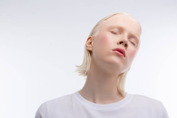 Skinny young model with rosy cheeks closing eyes while posing Rosy cheeks. Skinny young model with rosy cheeks closing eyes while posing near white wall pale complexion stock pictures, royalty-free photos & images