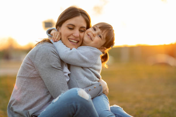 Little girl embracing her mom in the nature. Mother holding flower bouquet