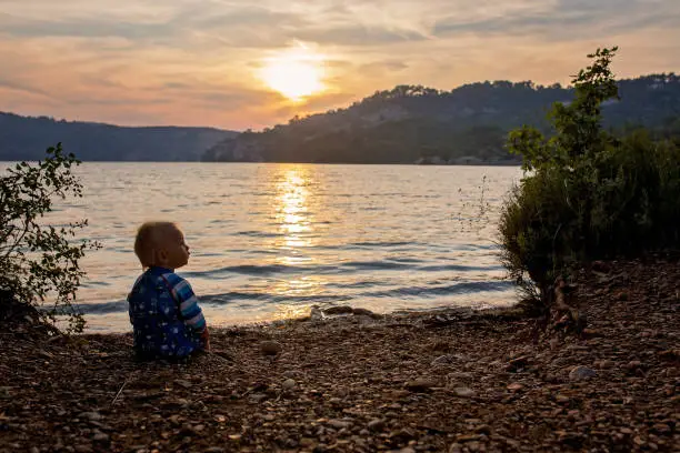 Photo of Cute child, toddler boy, enjoying the sunset over a lake