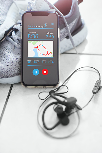 Mobile phone and headphones resting against a pair of trainers. The screen is displaying a fitness app showing the users run details.