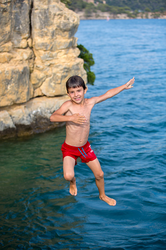 Boy jumping to the lake. Child jumping off a cliff into the sea. Summer fun lifestyle