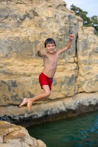 Photo of Boy jumping to the lake. Child jumping off a cliff into the sea. Summer fun