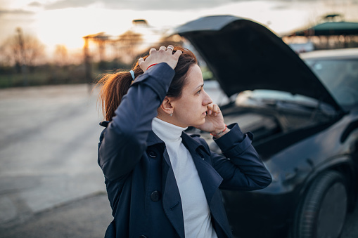 Young, stressed woman is calling emergency service  to help her with a broken car.