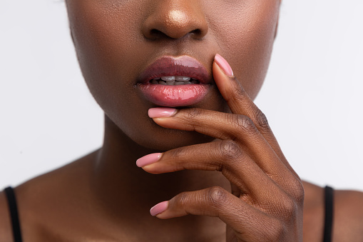Shiny lip gloss. Close up of young African-American woman touching lips with shiny lip gloss
