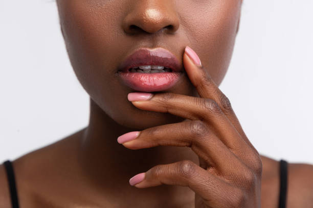 African-American woman touching lips with shiny lip gloss Shiny lip gloss. Close up of young African-American woman touching lips with shiny lip gloss african young lips closeup stock pictures, royalty-free photos & images