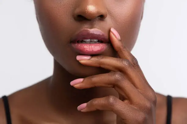 Photo of African-American woman touching lips with shiny lip gloss