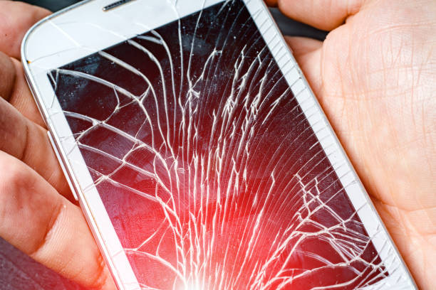 istock White modern smart phone with broken touch screen isolated on male's hand with red light leaks. 1141301435