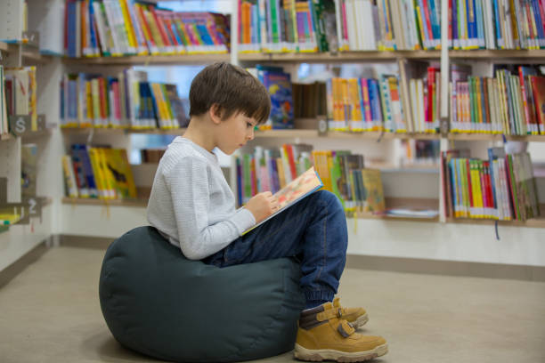 istock Smart toddler boy, educating himself in a library, reading books 1141301633