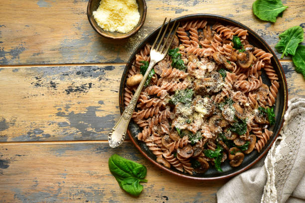 Whole wheat fusilli pasta with mushroom and spinach Whole wheat fusilli pasta with mushroom and spinach on a dark plate over old rustic wooden background.Top view with copy space. fusilli stock pictures, royalty-free photos & images