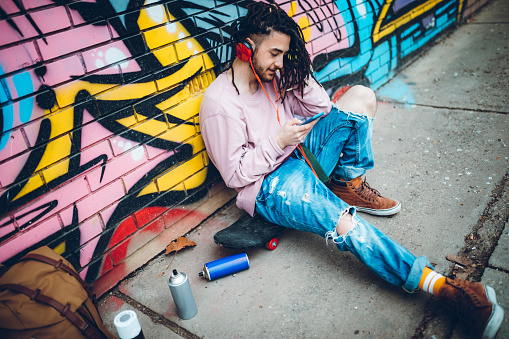 Young man with dreadlocks is listening to music and using mobile phone