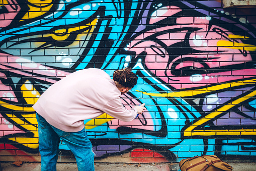 Young man with dreadlocks is painting graffiti with spray paint