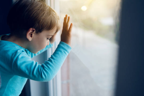 kleiner junge zu hause schaut durch das fenster und wartet darauf, dass seine mutter wieder nach hause kommt - approaching stock-fotos und bilder