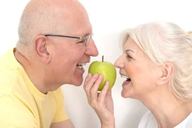 Senior couple with green apple. Healthy teeth, strong dentures, healthy nutrition concept
