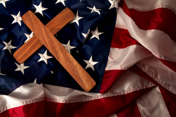 Evangelical America, Christianity, born again Christian and fundamentalist religious right concept with close up on a wooden cross or crucifix on the American flag with dramatic light and moody tone Evangelical America, christianity, born again christian and fundamentalist religious right concept with close up on a wooden cross or crucifix on the american flag with dramatic light and moody tone evangelic stock pictures, royalty-free photos & images