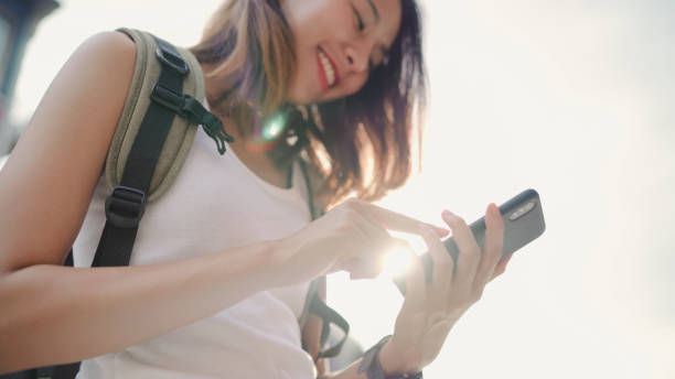 Cheerful Asian backpacker blogger woman using smartphone for direction and looking on location map while traveling at Chinatown in Beijing, China. Lifestyle backpack tourist travel holiday concept.