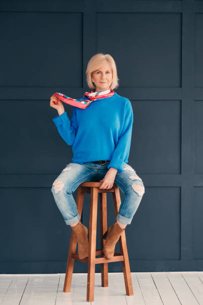senior model woman beauty elegance confidence blue Senior model. Woman beauty. Attractive aged lady sitting on bar stool. Elegance and confidence. Trendy blue outfit. womens blue suede shoes stock pictures, royalty-free photos & images