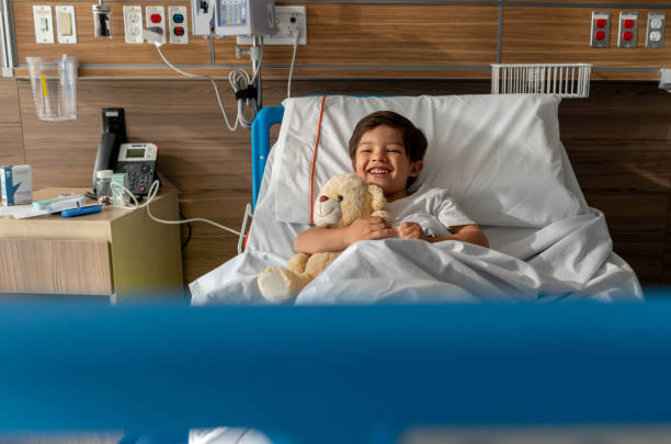 istock Cute little boy laughing and huggging his teddy bear while lying down on hospital bed 1141330654