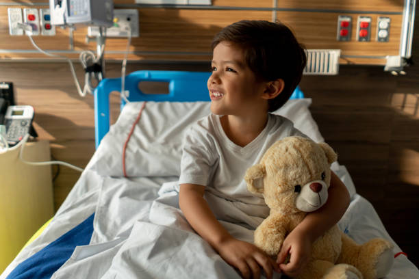 istock Cute boy sitting down on hospital bed hugging his teddy bear smiling 1141330660
