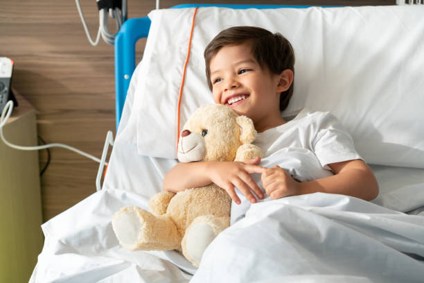 Happy little boy hugging his teddy bear while laughing and lying down on hospital bed Happy little boy hugging his teddy bear while laughing and lying down on hospital bed - Healthcare concepts teddy bear photos stock pictures, royalty-free photos & images