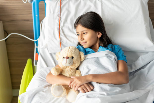 istock Hospitalized sweet girl lying down on bed looking away while hugging her teddy bear 1141330677