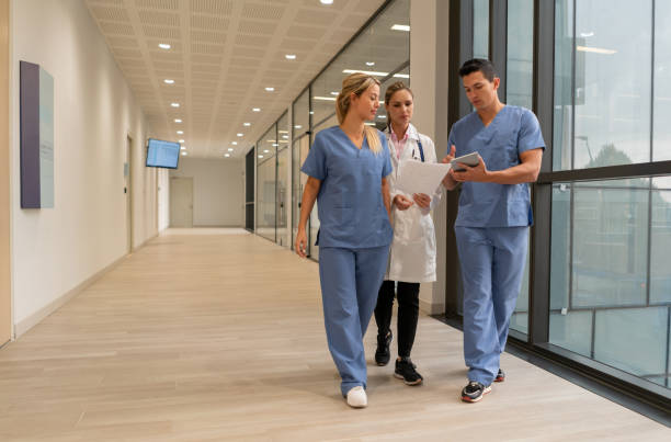 Medical residents showing something to female doctor on tablet while walking at the hospital Medical residents showing something to female doctor on tablet while walking at the hospital - Healthcare concepts civilian stock pictures, royalty-free photos & images
