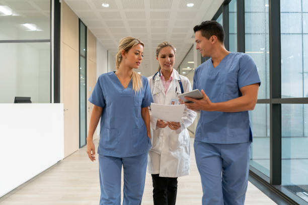 Team of nurses talking with doctor while showing something on tablet and walking down the corridor of the hospital