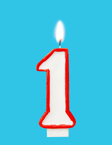 Burning wax candle for a birthday cake in the form of number one. Blue background