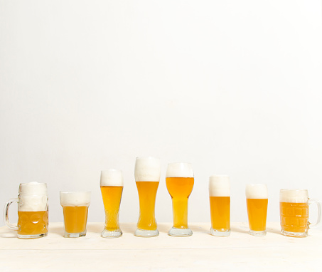 Glasses with different sorts of craft beer on wooden bar. Tap beer in pint glasses arranged in a row. Closeup of five glasses of different types of draught beer in a pub.