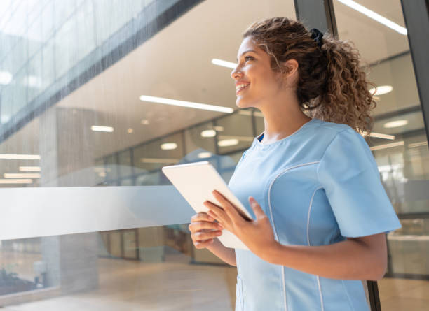 istock Thoughtful but cheerful nurse looking through the window smiling and holding a tablet 1141333728
