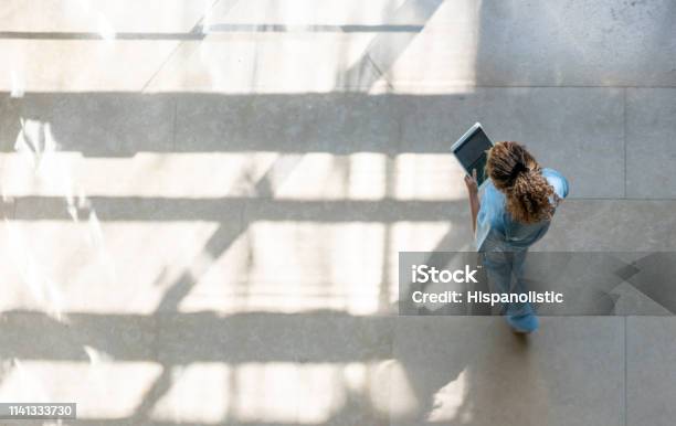High Angle View Of Nurse Walking Around Hospital While Looking At A Medical Chart On Tablet Stock Photo - Download Image Now