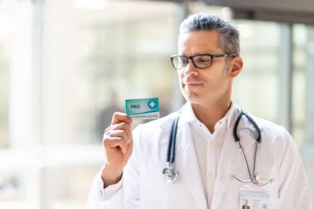 Photo of Male practitioner at the hospital holding an insurance card while looking at it