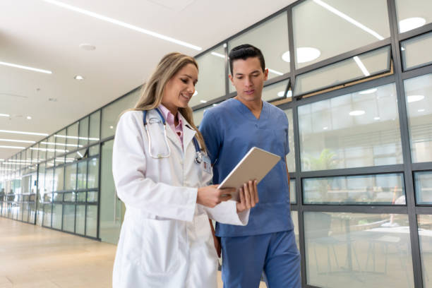 Handsome male nurse talking with female doctor while both are looking at a tablet walking through the corridor Handsome male nurse talking with female doctor while both are looking at a tablet walking through the corridor - Healthcare concepts civilian stock pictures, royalty-free photos & images