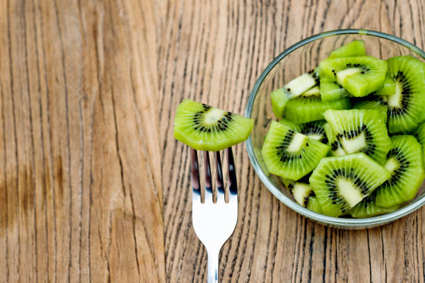 A plate of kiwi fruit slices with fork on wooden table.
