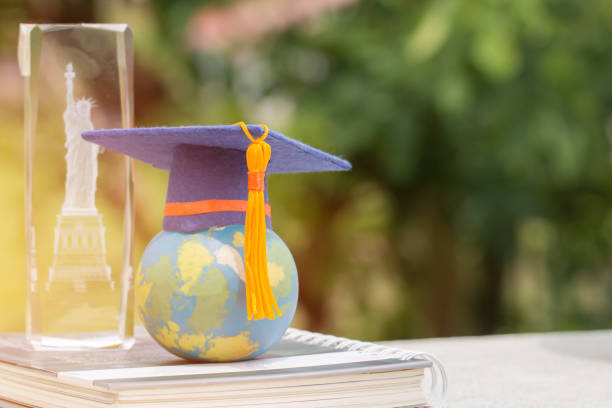 istock Learning study international abroad in America concept: Graduate cap on earth world globe model map on book with blur of USA Statue of Liberty crystal souvenir. Idea of Work and Travel studies program 1141338011
