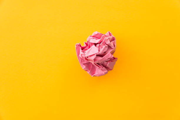 Pink crumpled paper ball on yellow background.