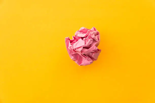 Photo of Pink crumpled paper ball on yellow background
