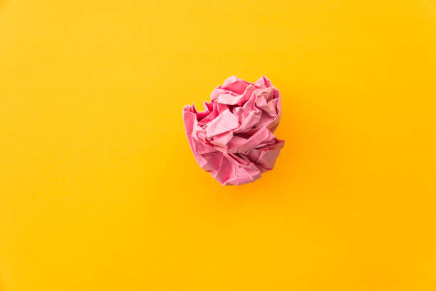 pink crumpled paper ball on yellow background - crumpled paper document frustration imagens e fotografias de stock