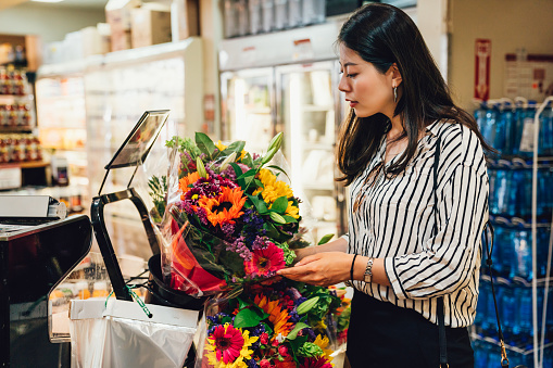 Young asian woman holding beautiful fresh blossom colorful flowers in supermarket. Shopping consumerism people concept. elegant lady love plants floral hobby buying to decorate home apartment.