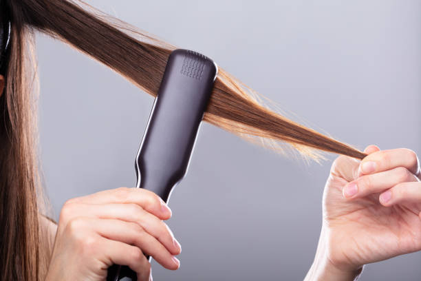 mujer enderezando el cabello con el enderezador - straightener fotografías e imágenes de stock