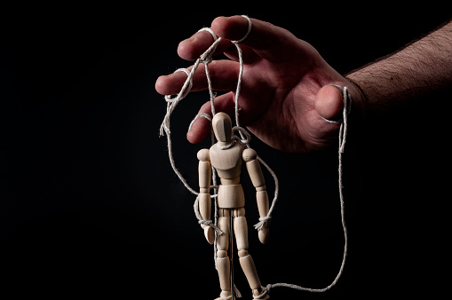 Employer manipulating the employee, personality disorder , emotional manipulation and obey the master concept with ominous hand pulling the strings on a marionette with moody contrast on black background