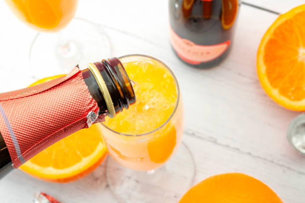 bebidas exuberantes, bebidas alcohólicas de verano y un refrescante concepto de cóctel con brunch mimosa con vista superior de frutas anaranjadas y champán que se vierte de una botella de burbujeante aislado sobre un fondo de mesa de madera - brunch fotografías e imágenes de stock