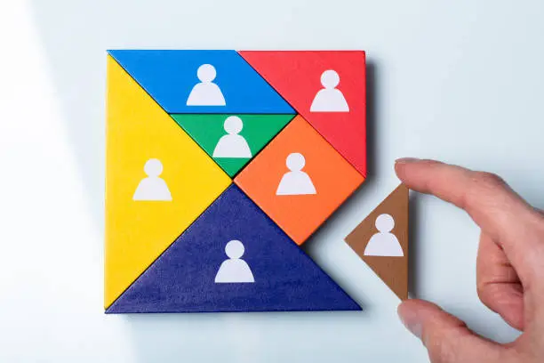 An Overhead View Of Person's Hand Holding A Missing Piece In A Square Tangram Puzzle