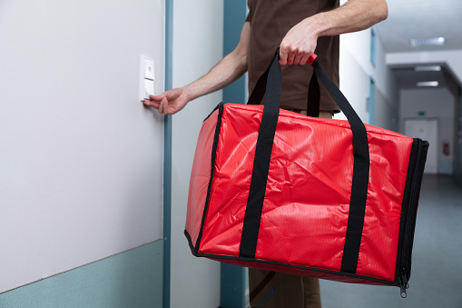 Pizza Delivery Man Ringing The Door Bell With A Large Red Bag In His Hand