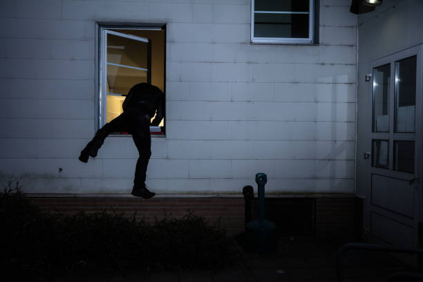 burglar entering in a house through a window - burglary imagens e fotografias de stock