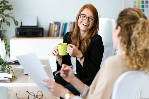 zwei hübsche junge geschäftsfrau entspannen sich einen moment beim kaffeetrinken im büro. - business women computer cheerful stock-fotos und bilder